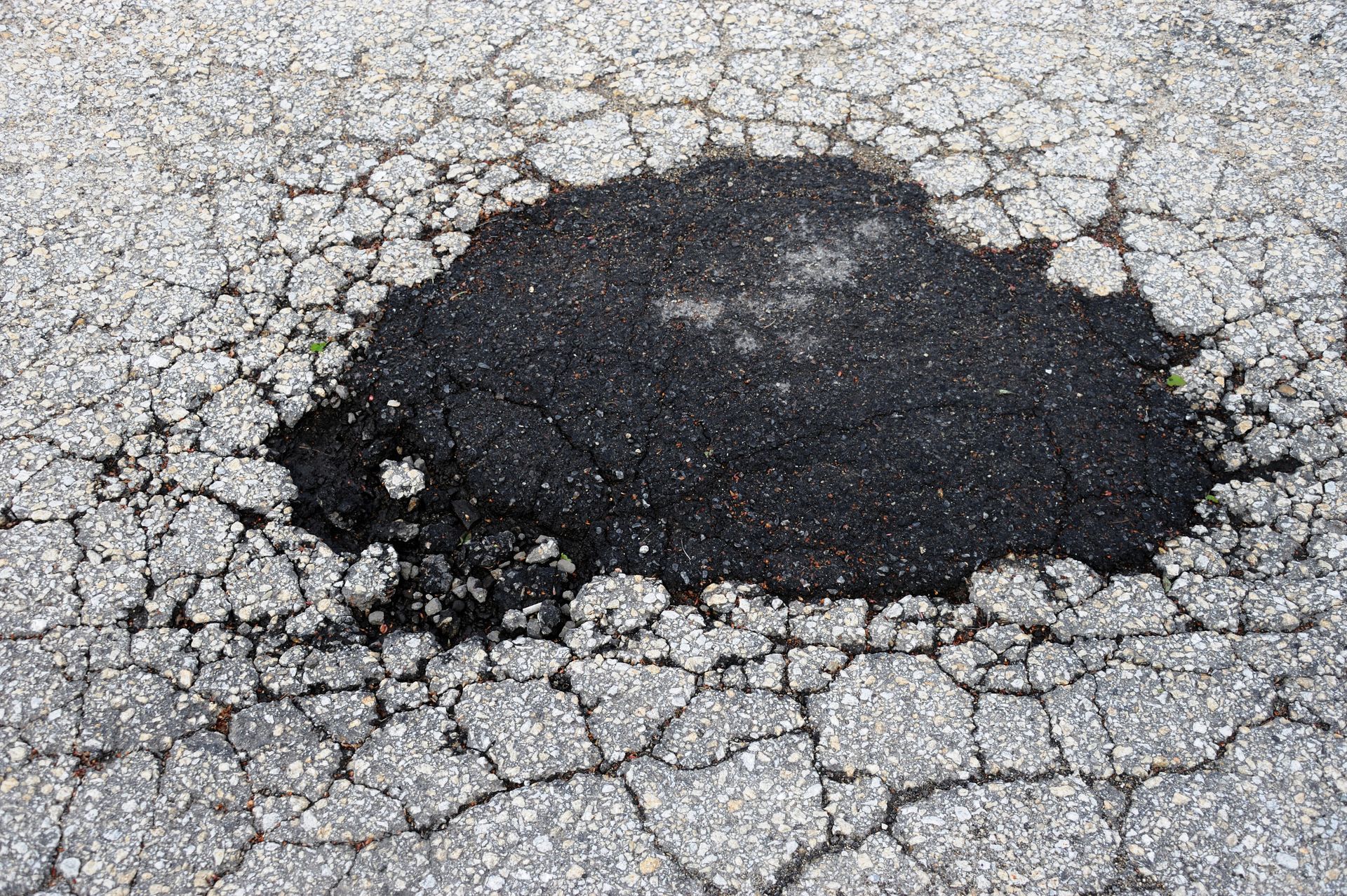 Pothole in asphalt road, surrounded by cracked pavement. Dark asphalt fills the hole. Pothole in asphalt road, surrounded by cracked pavement. Dark asphalt fills the hole.