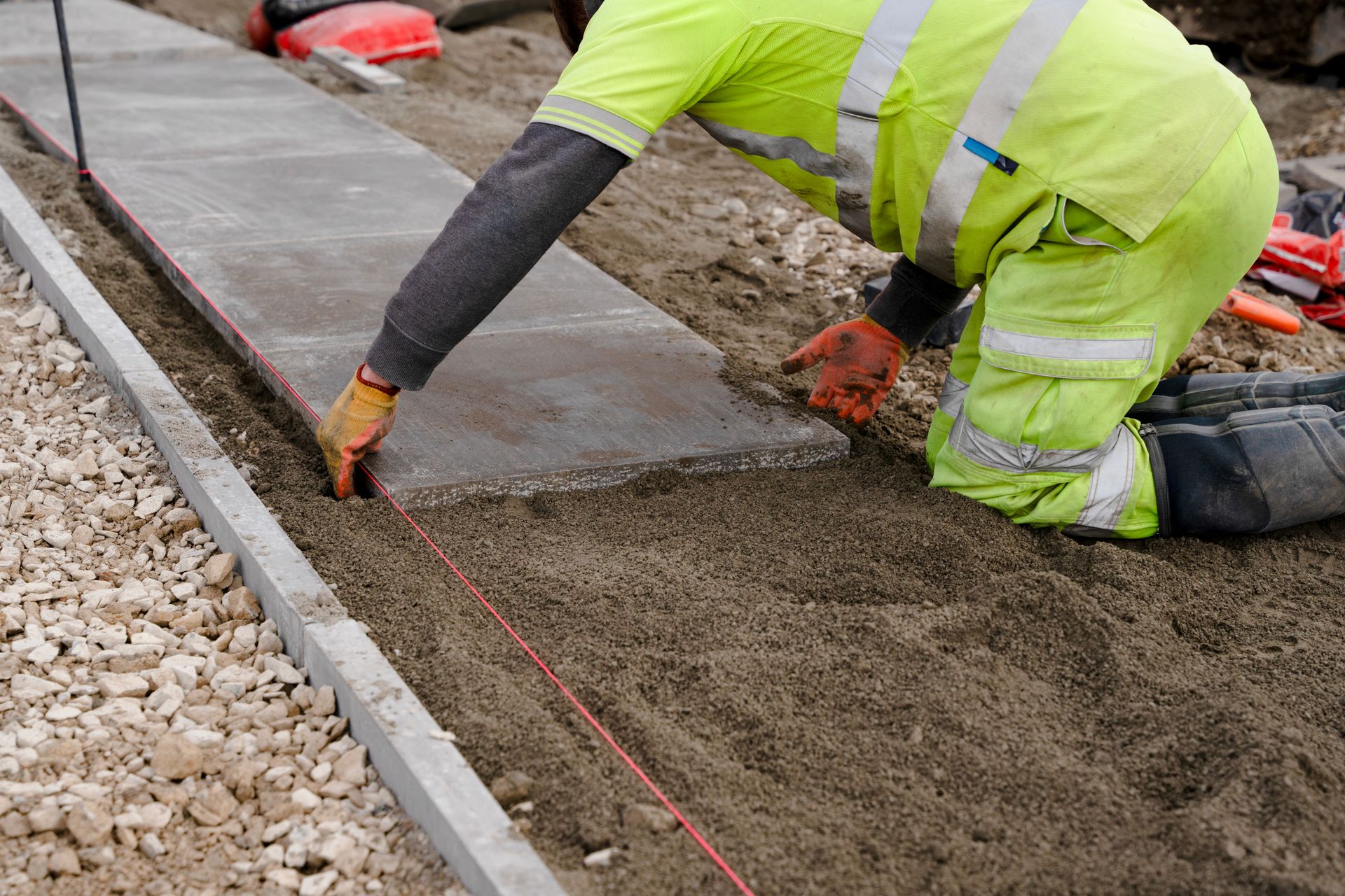 Construction worker laying a stone pavement on a sand base, guided by a string, wearing safety gear. Construction worker laying a stone pavement on a sand base, guided by a string, wearing safety gear.