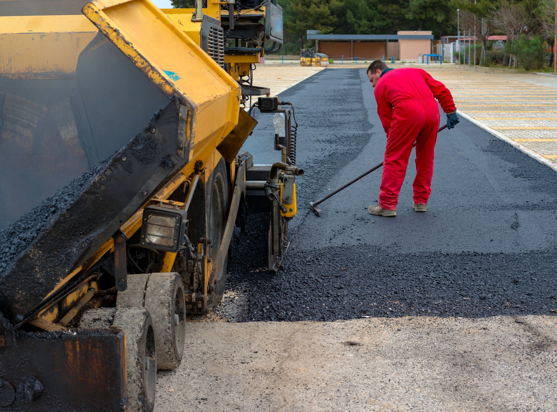 Asphalt paving machine laying asphalt; worker raking the fresh asphalt on a parking lot. Asphalt paving machine laying asphalt; worker raking the fresh asphalt on a parking lot.