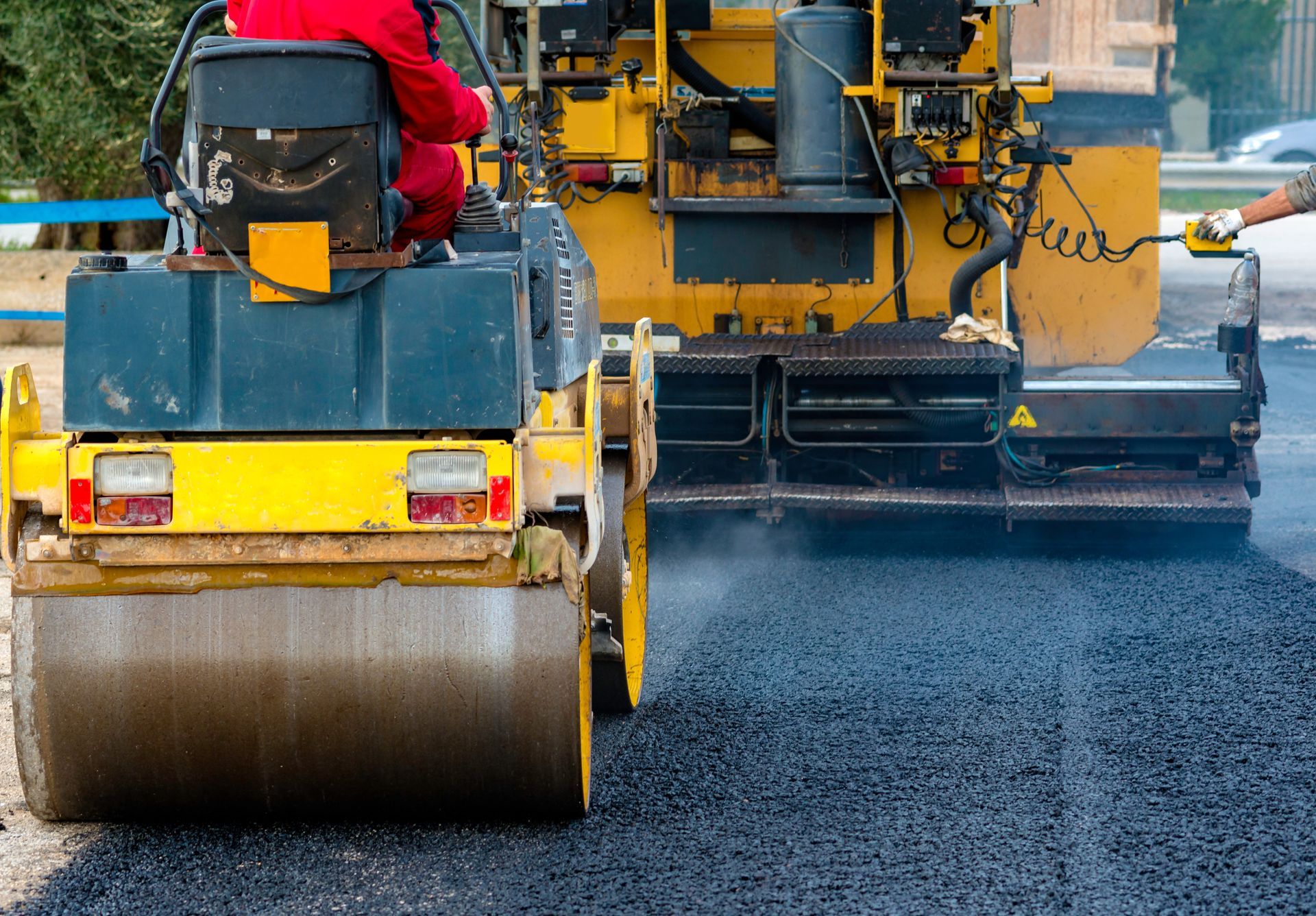 Road roller compacting fresh asphalt on a road; yellow and black machinery with a person operating it. Road roller compacting fresh asphalt on a road; yellow and black machinery with a person operating it.