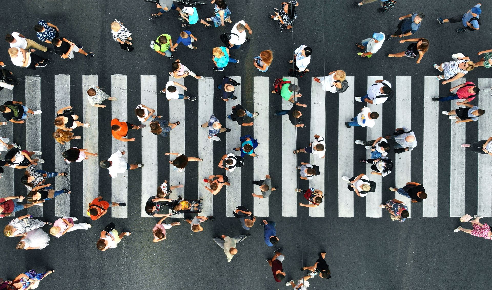 Aerial view of many people walking across a zebra-striped crosswalk.