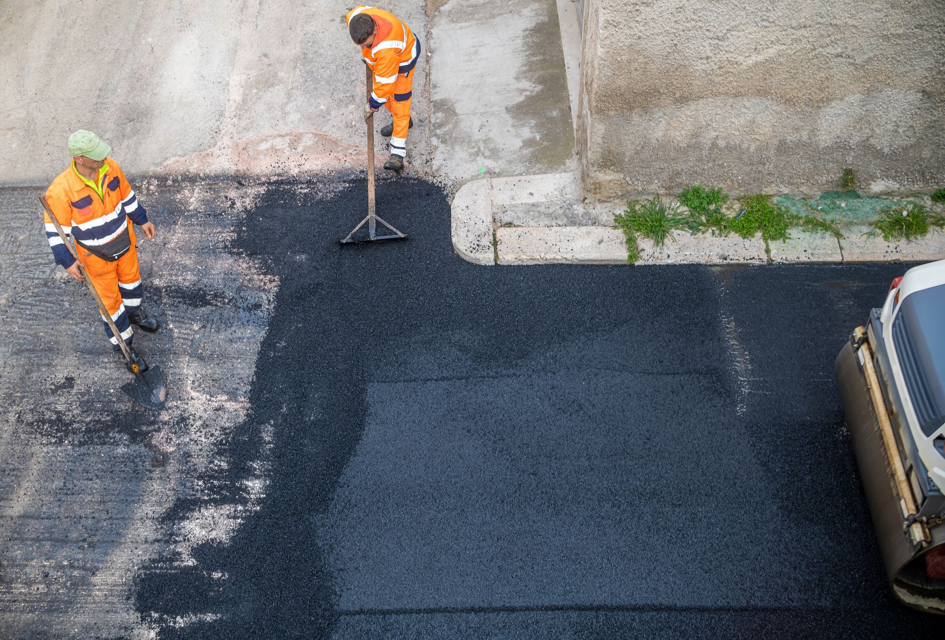 Two workers in orange vests paving a road section with black asphalt. Two workers in orange vests paving a road section with black asphalt.