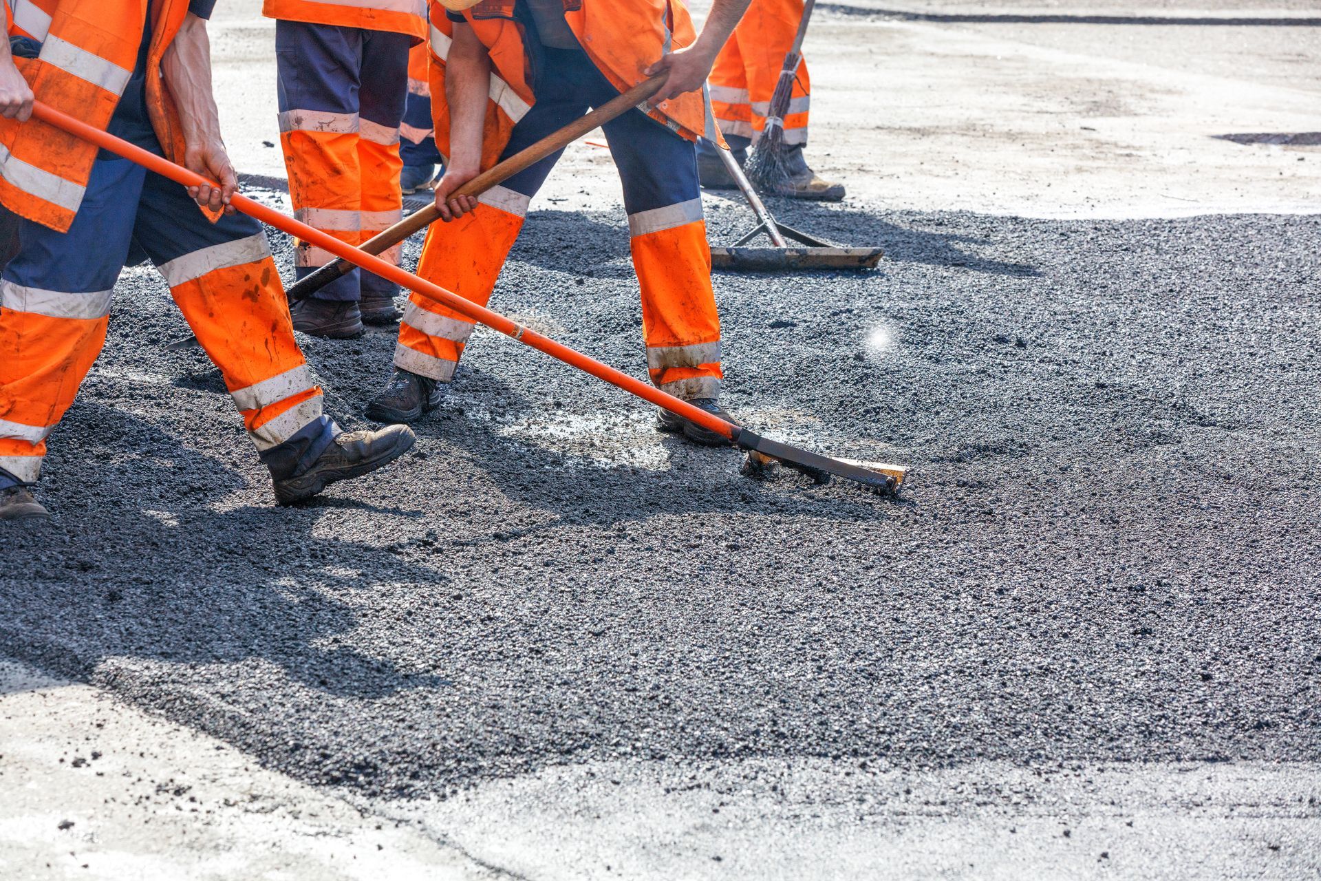 Construction workers in orange vests and pants spreading asphalt with rakes on a road. Construction workers in orange vests and pants spreading asphalt with rakes on a road.
