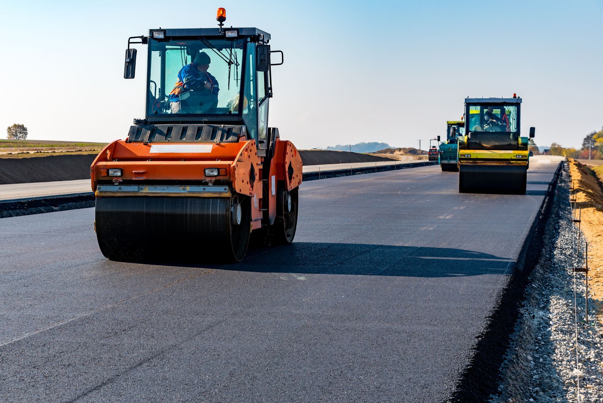 Road rollers compacting fresh asphalt on a highway under construction. Blue sky. Road rollers compacting fresh asphalt on a highway under construction. Blue sky.