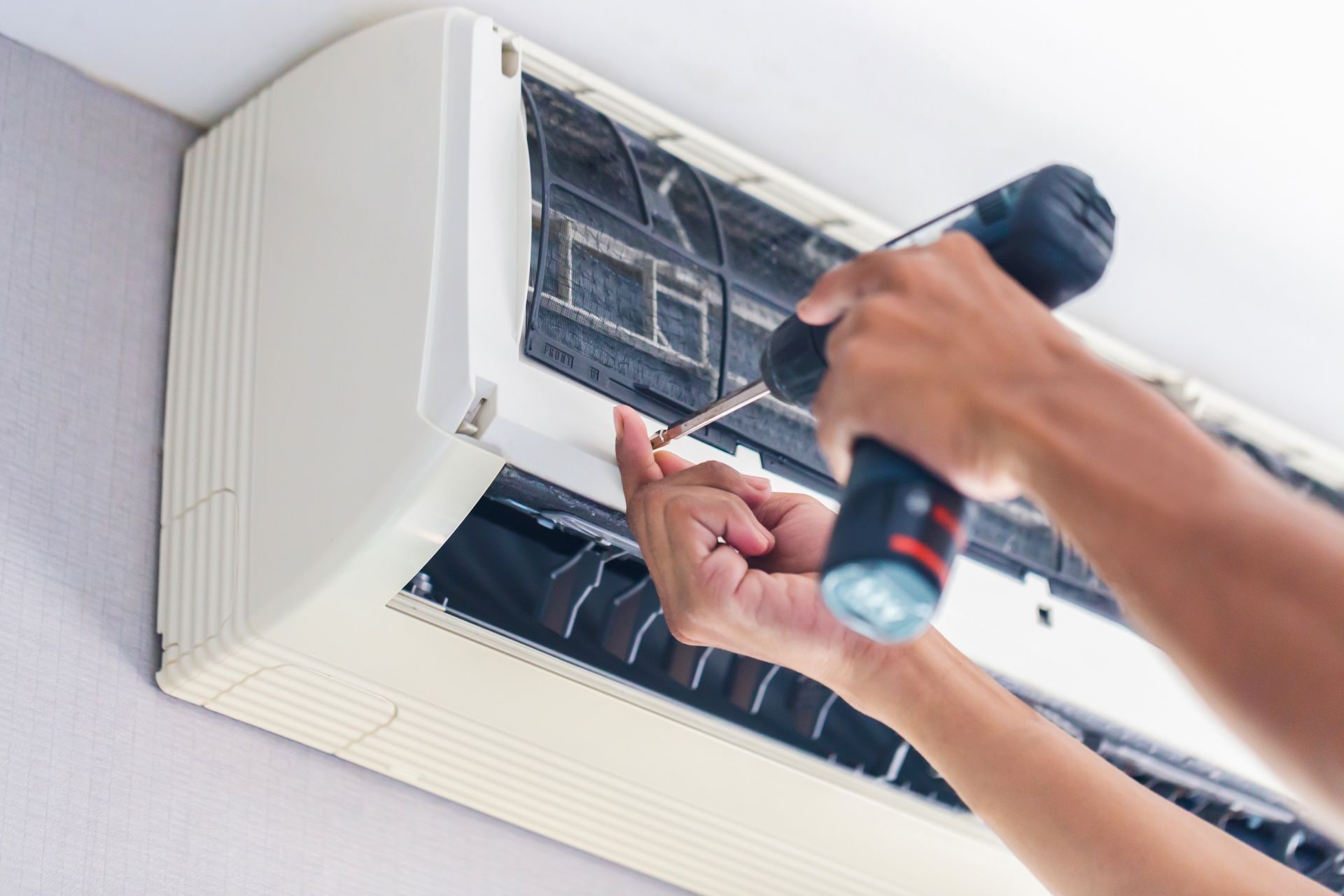 Technician cleaning a wall-mounted air conditioner with a screwdriver and spray bottle