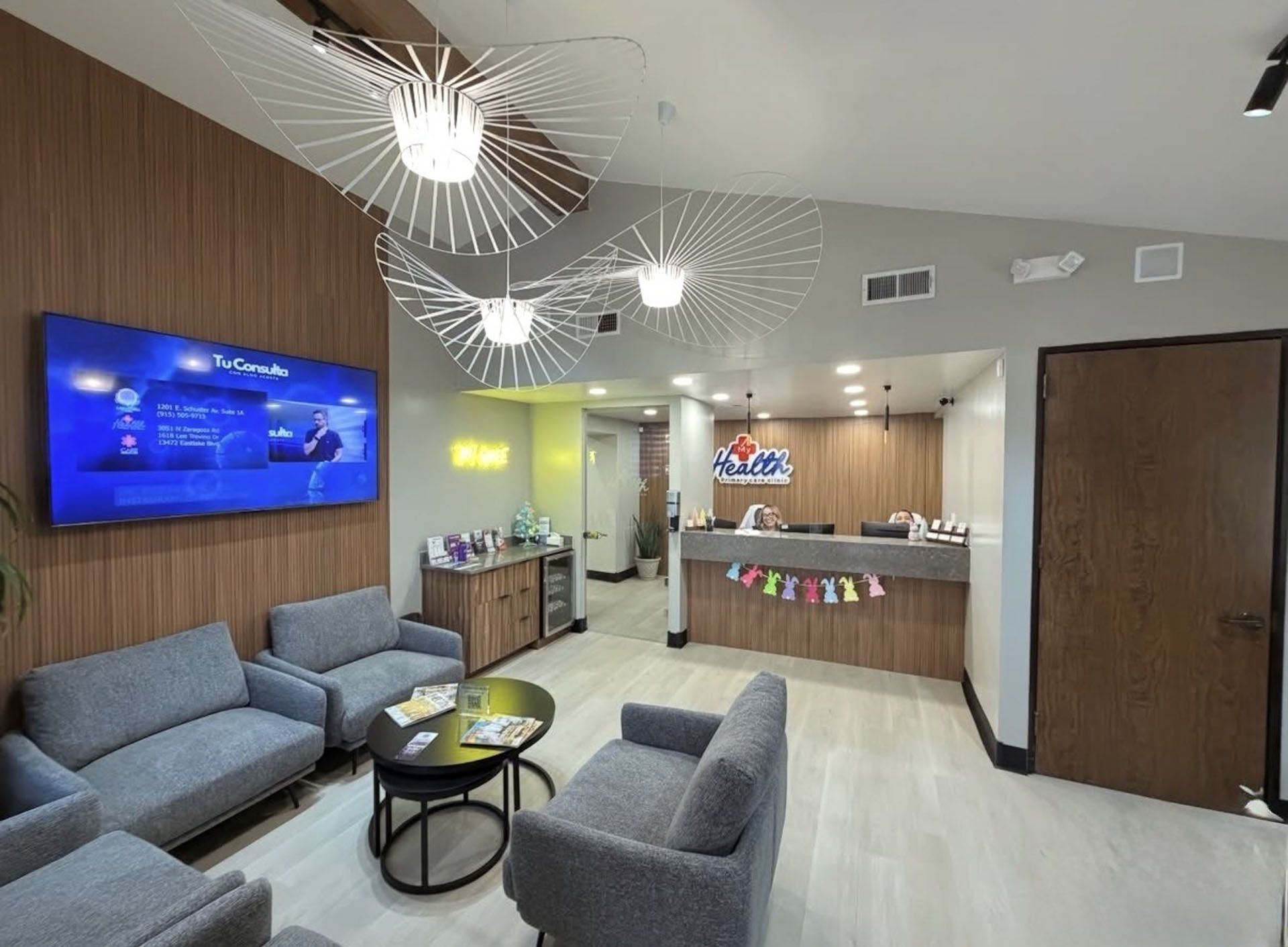 Modern office lobby with gray seating, blue TV screen, and reception desk