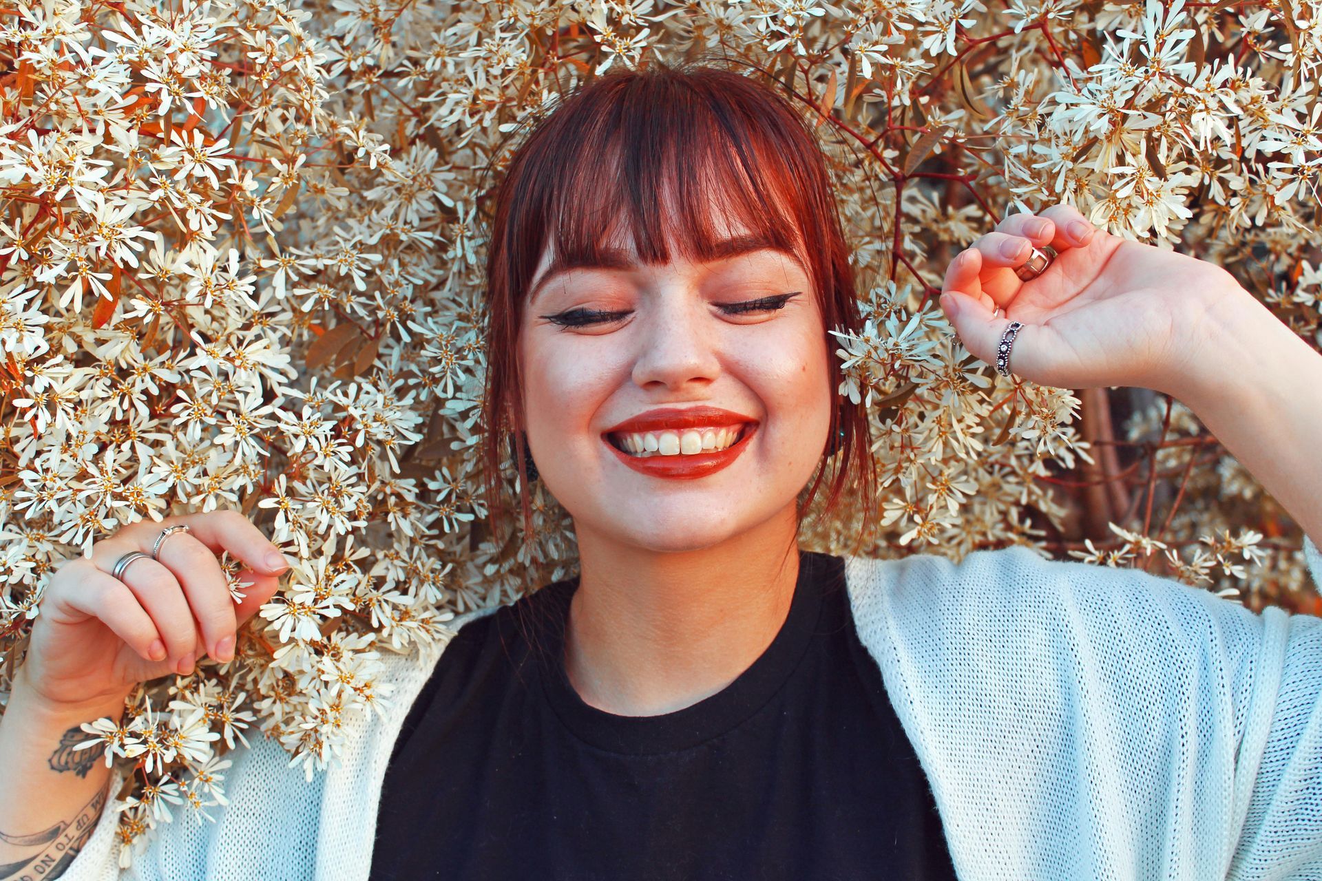 Woman smiles, eyes closed, against a backdrop of small white flowers.