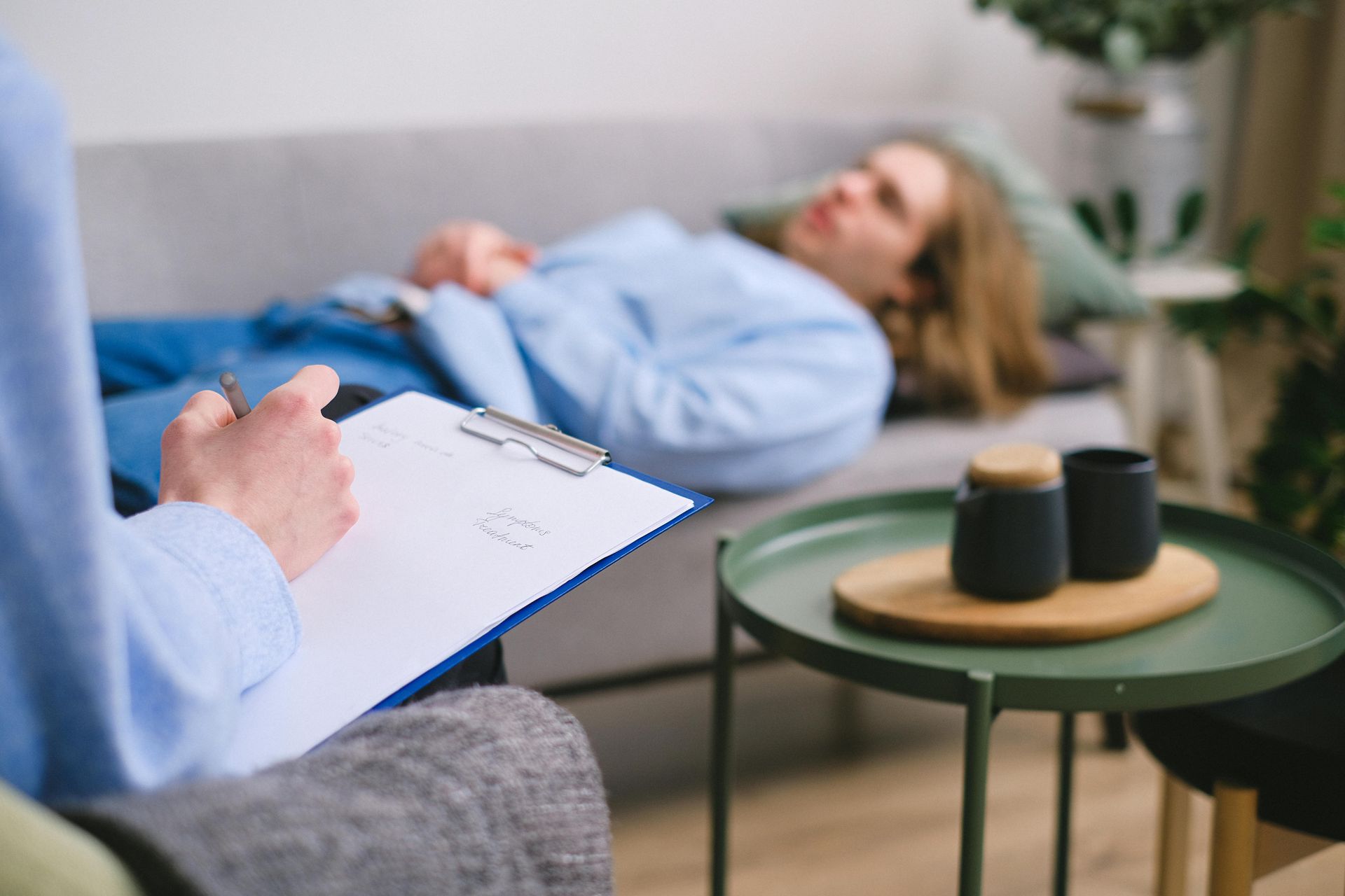 Therapist taking notes during a session with a person lying on a couch.