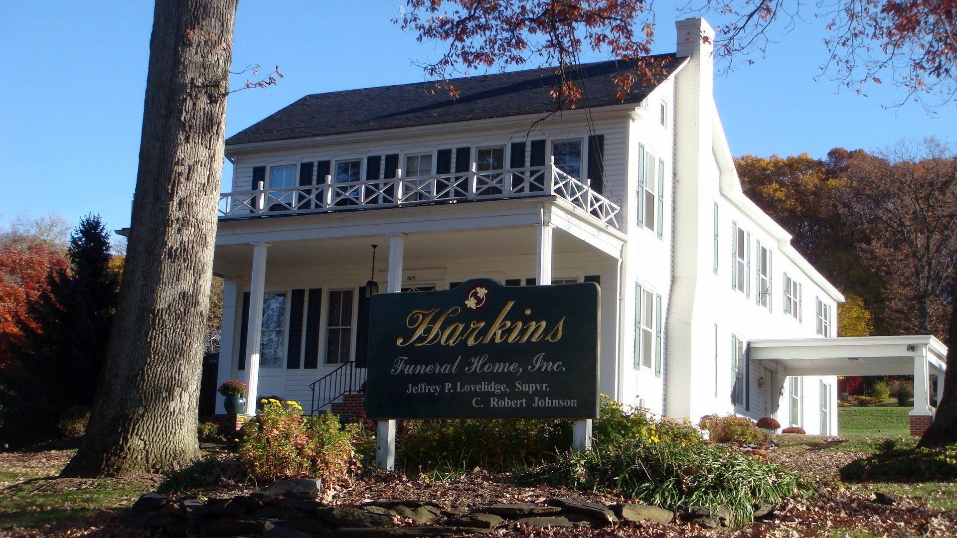 White Harkins's Funeral Home with a porch, sign, and trees.