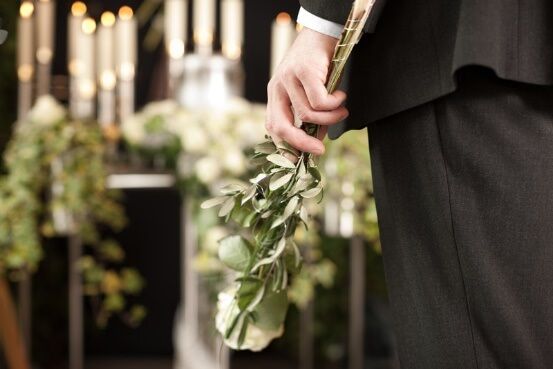 Person holding a floral tribute at a funeral service with candles and greenery.