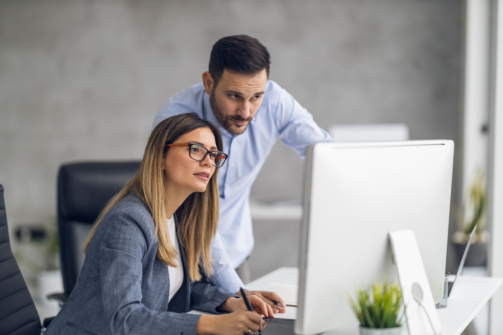 Woman and man working together at a computer in an office, looking at the screen.