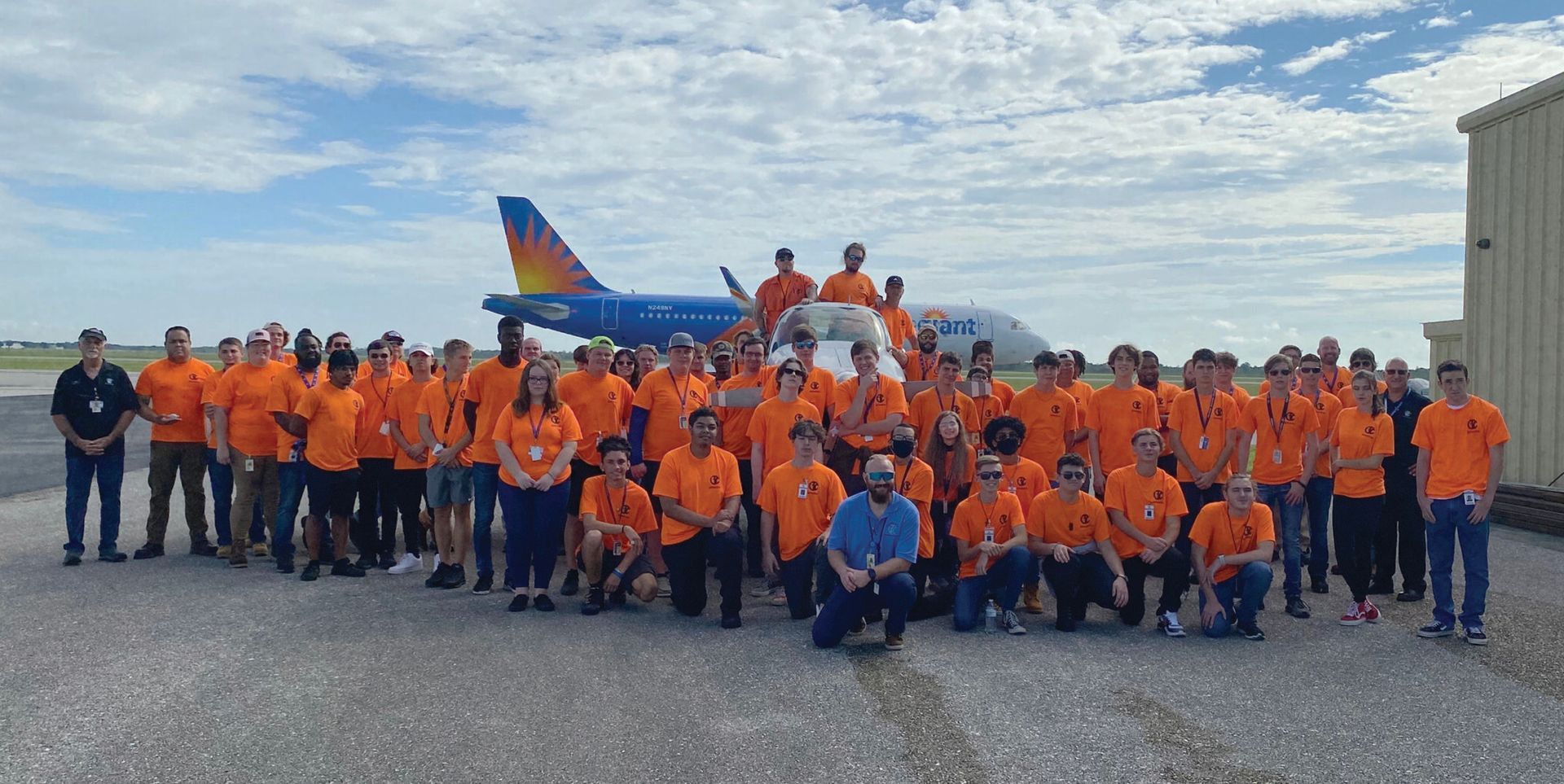 A large group of people are posing for a picture in front of an airplane.