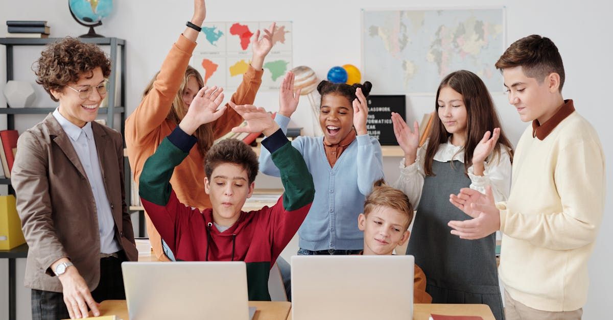 A group of children are standing around a table with laptops.