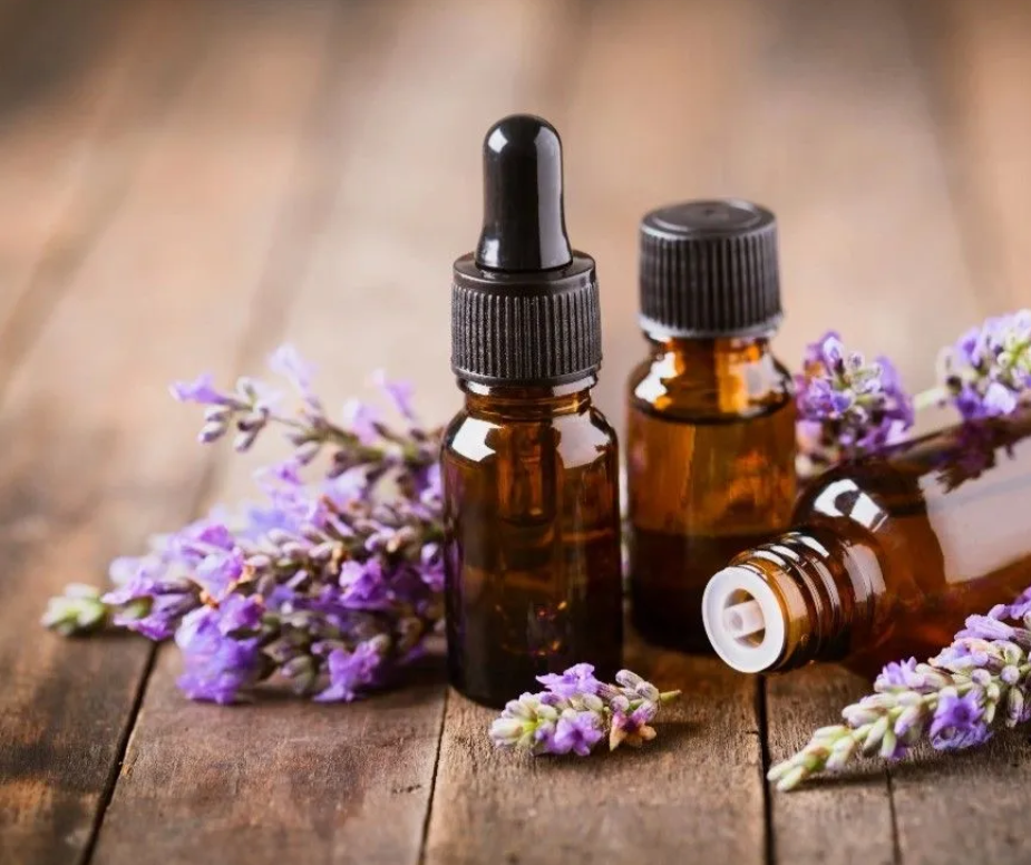 Three bottles of essential oil with purple flowers on a wooden table.