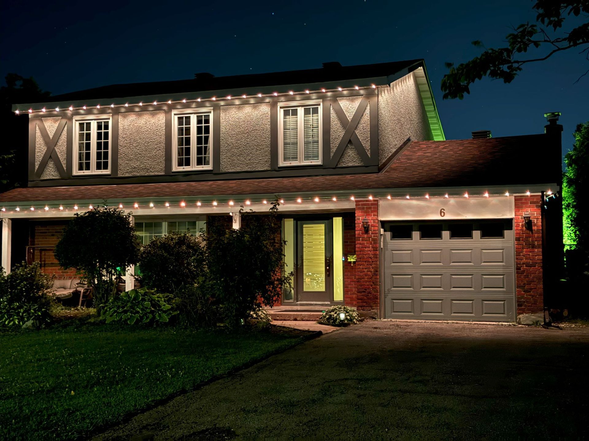 Two-story house at night with warm exterior lights, front lawn, and a lit garage door