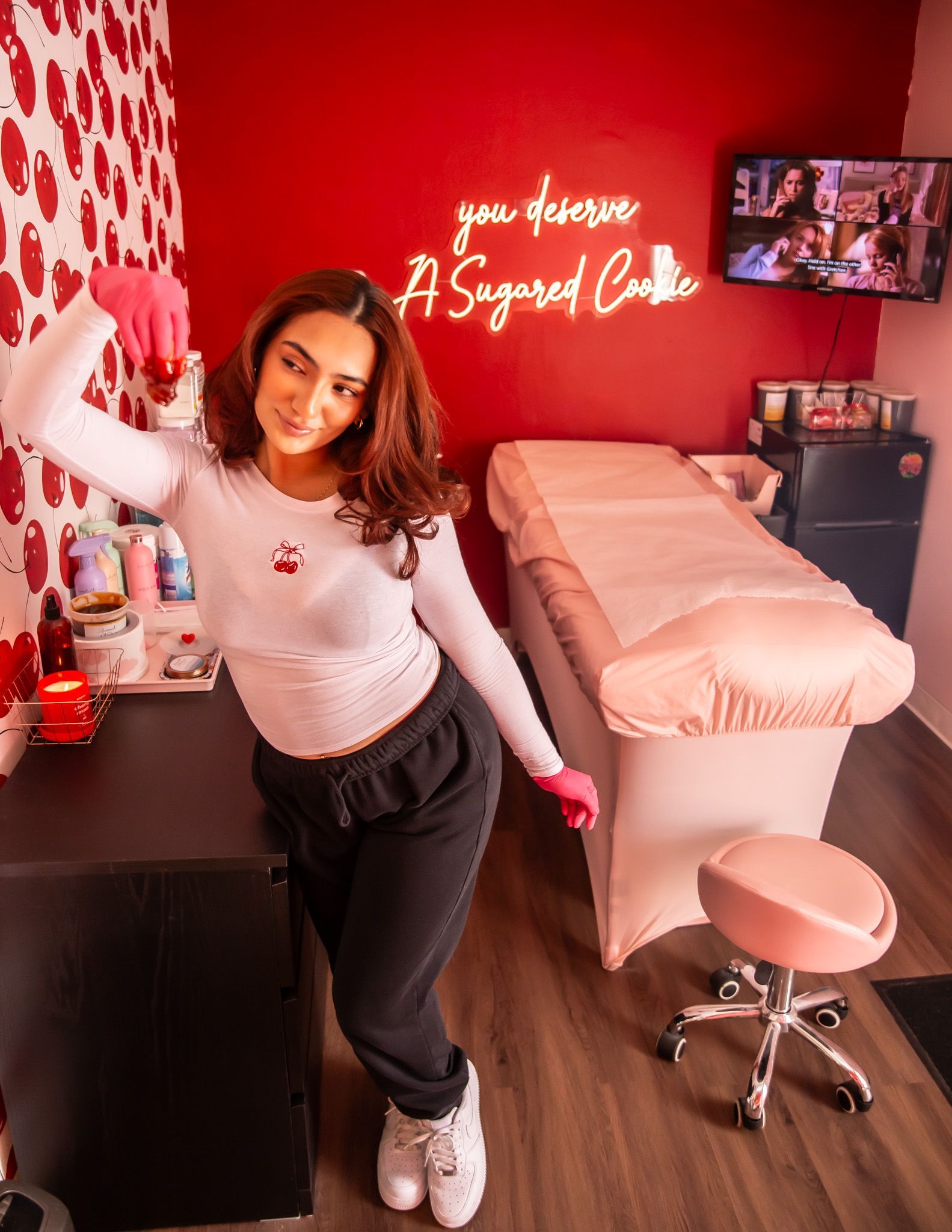 Woman in pink gloves and white shirt poses in a red-walled spa, next to a treatment bed.