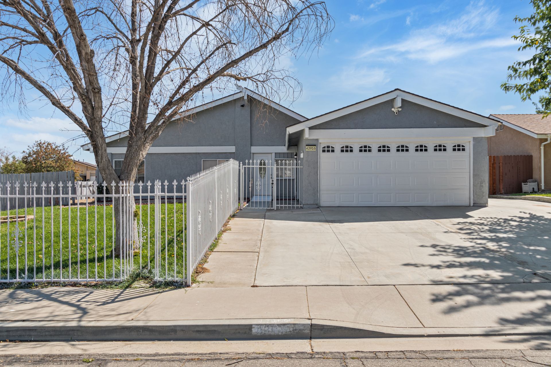 Gray house with white garage door and metal fence. Front yard with bare tree.