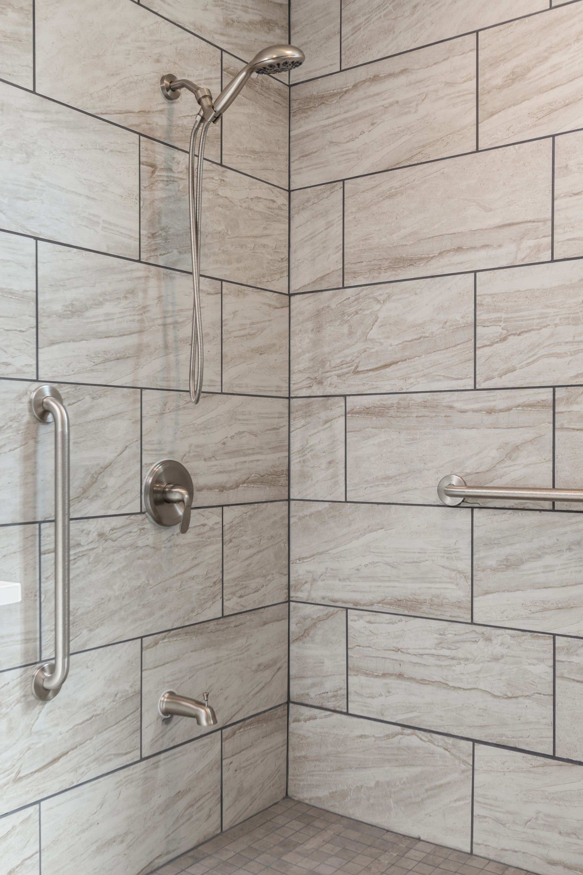 Tiled shower with grab bars. Silver fixtures and stone-look tiles.