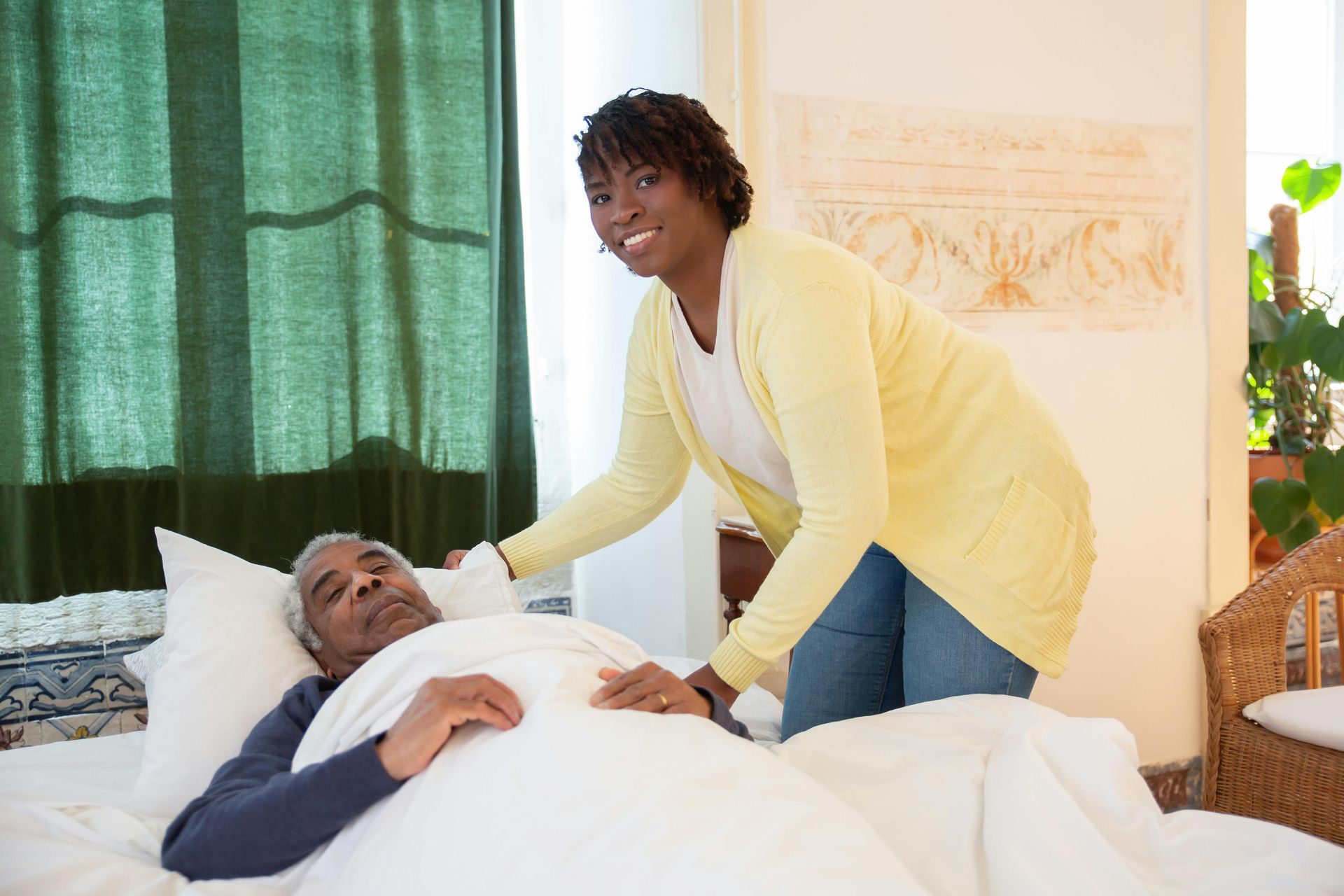 Woman assisting a person in bed, indoors.  Residential care facility for the elderly in Lancaster.