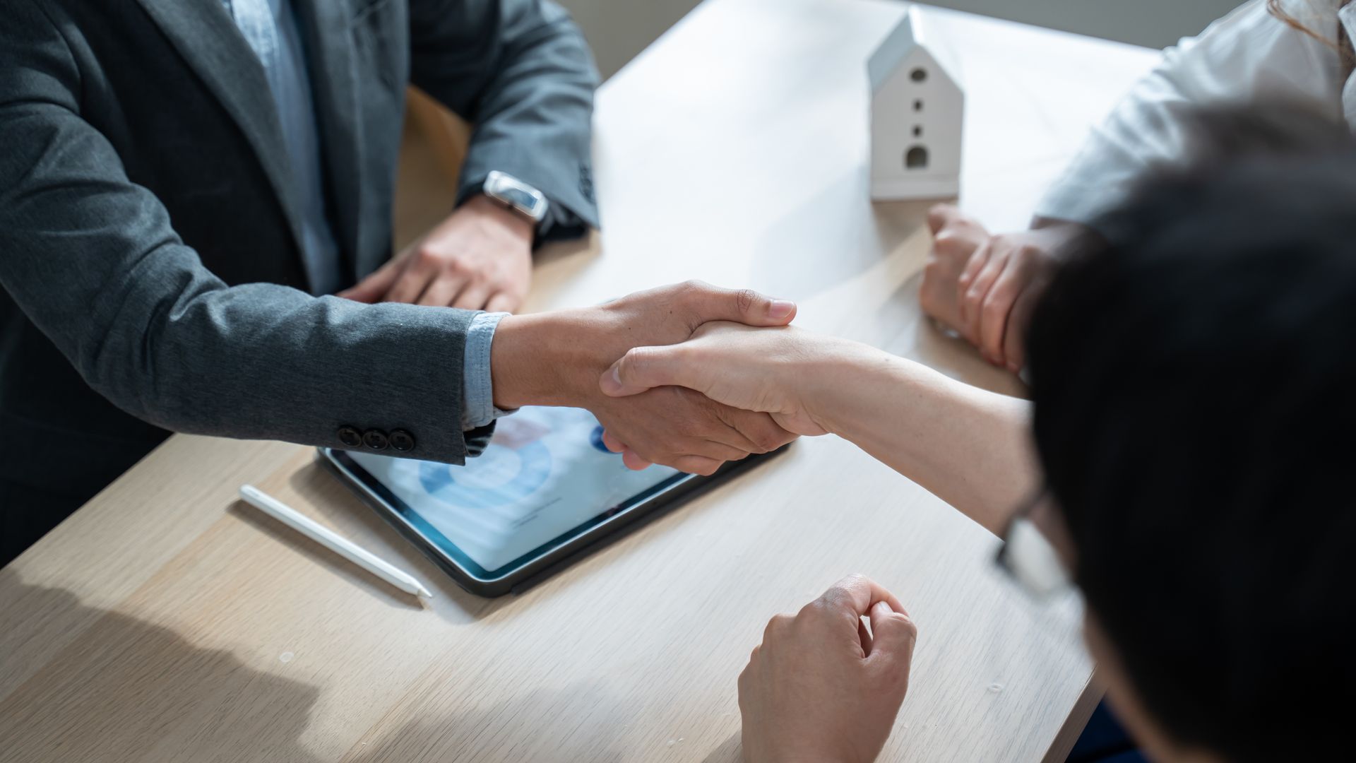 Two people shaking hands over a tablet at a business meeting table