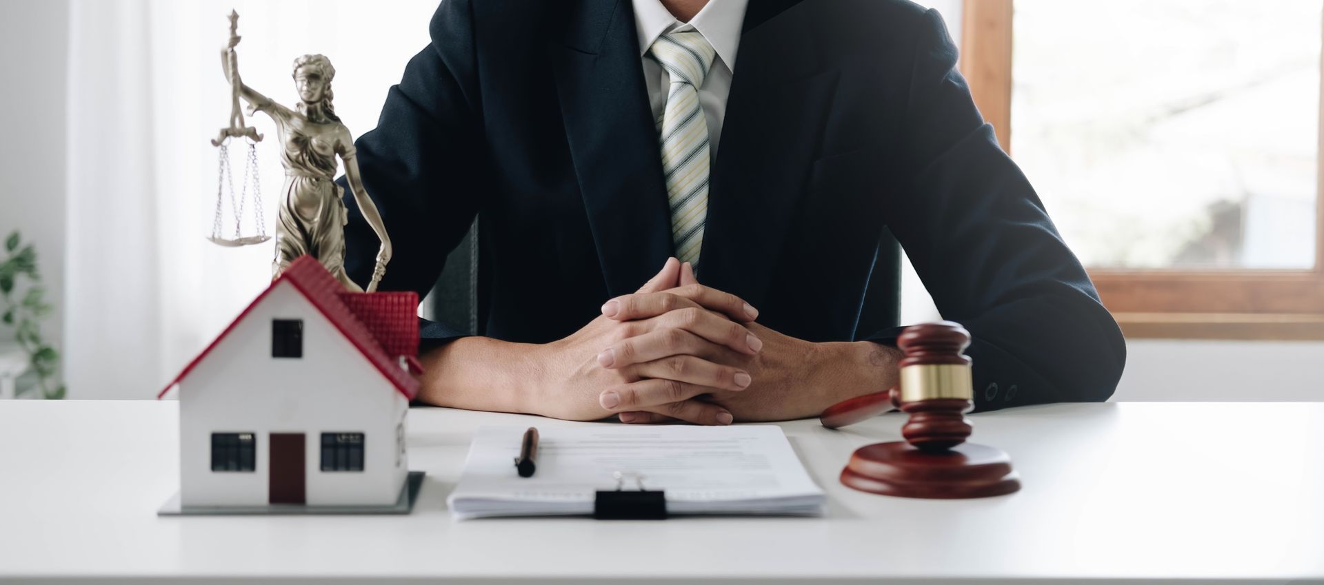 An estate attorney consults with a gavel, Lady Justice, and a house model on a desk. An estate attorney consults with a gavel, Lady Justice, and a house model on a desk.