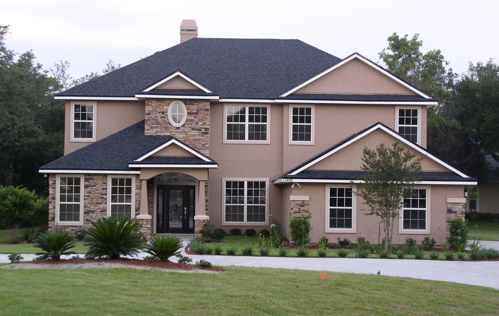 Two-story beige house with a dark gray roof and stone accents.