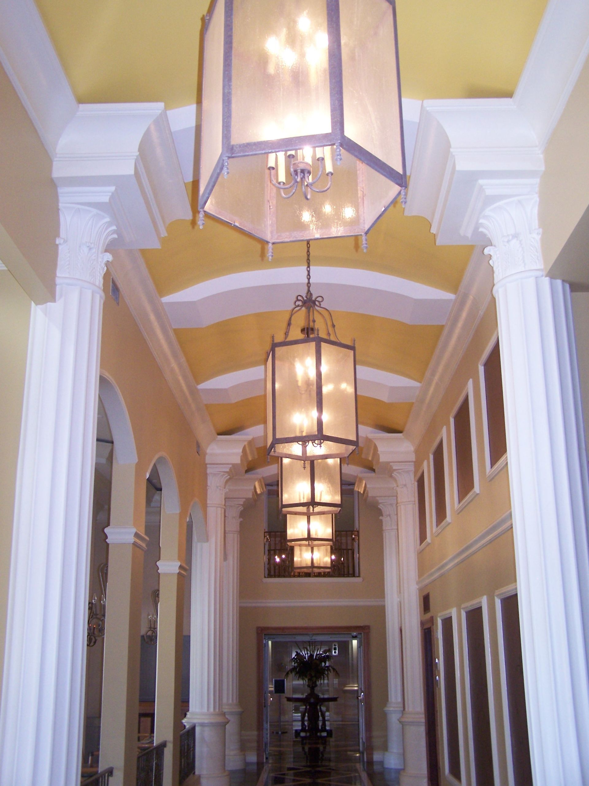 Long hallway with columns, arches, and hanging lamps. Yellow ceiling and walls, with dark floors.