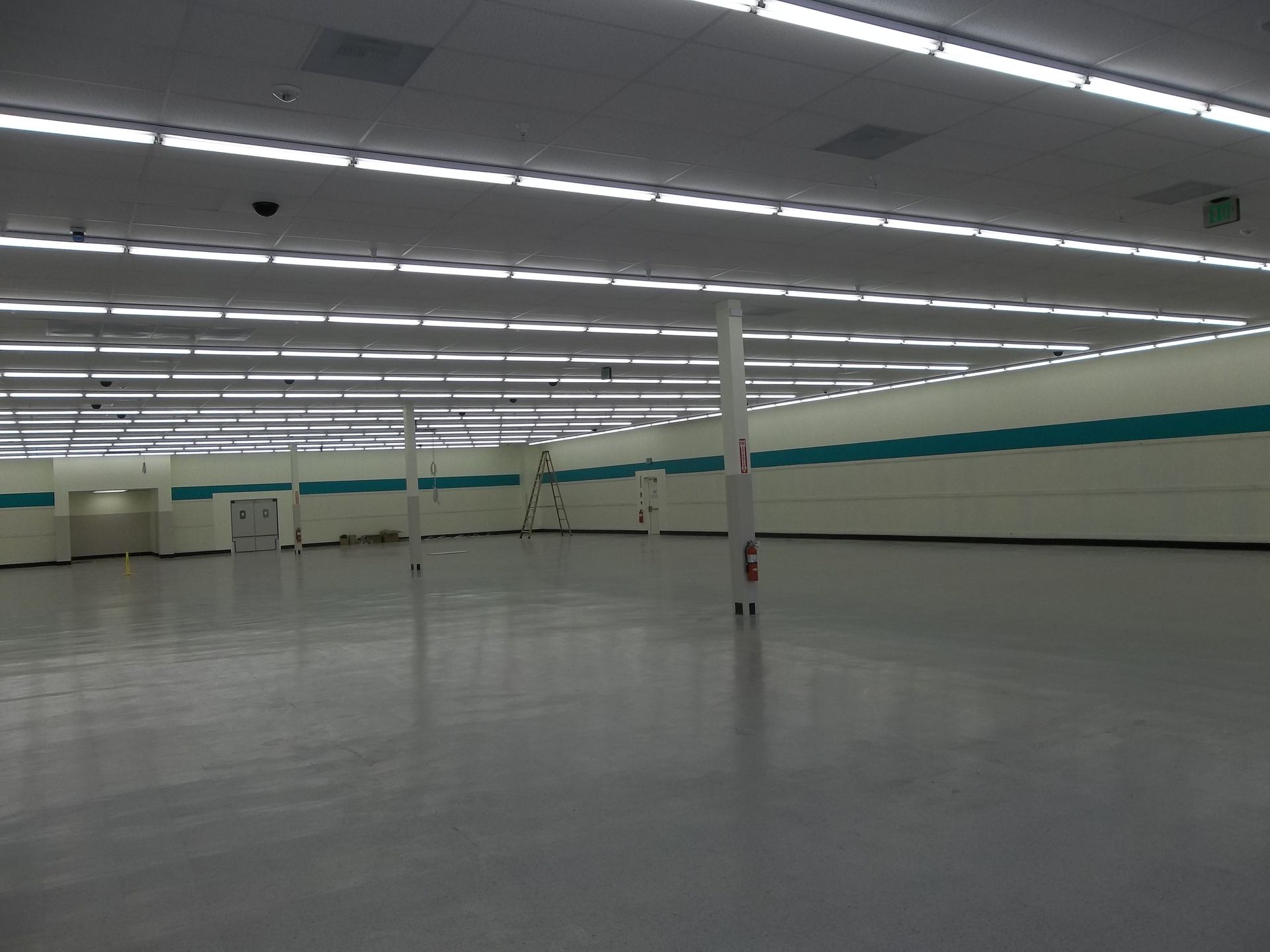 Empty, bright commercial space with gray floors, white walls, and teal stripe.