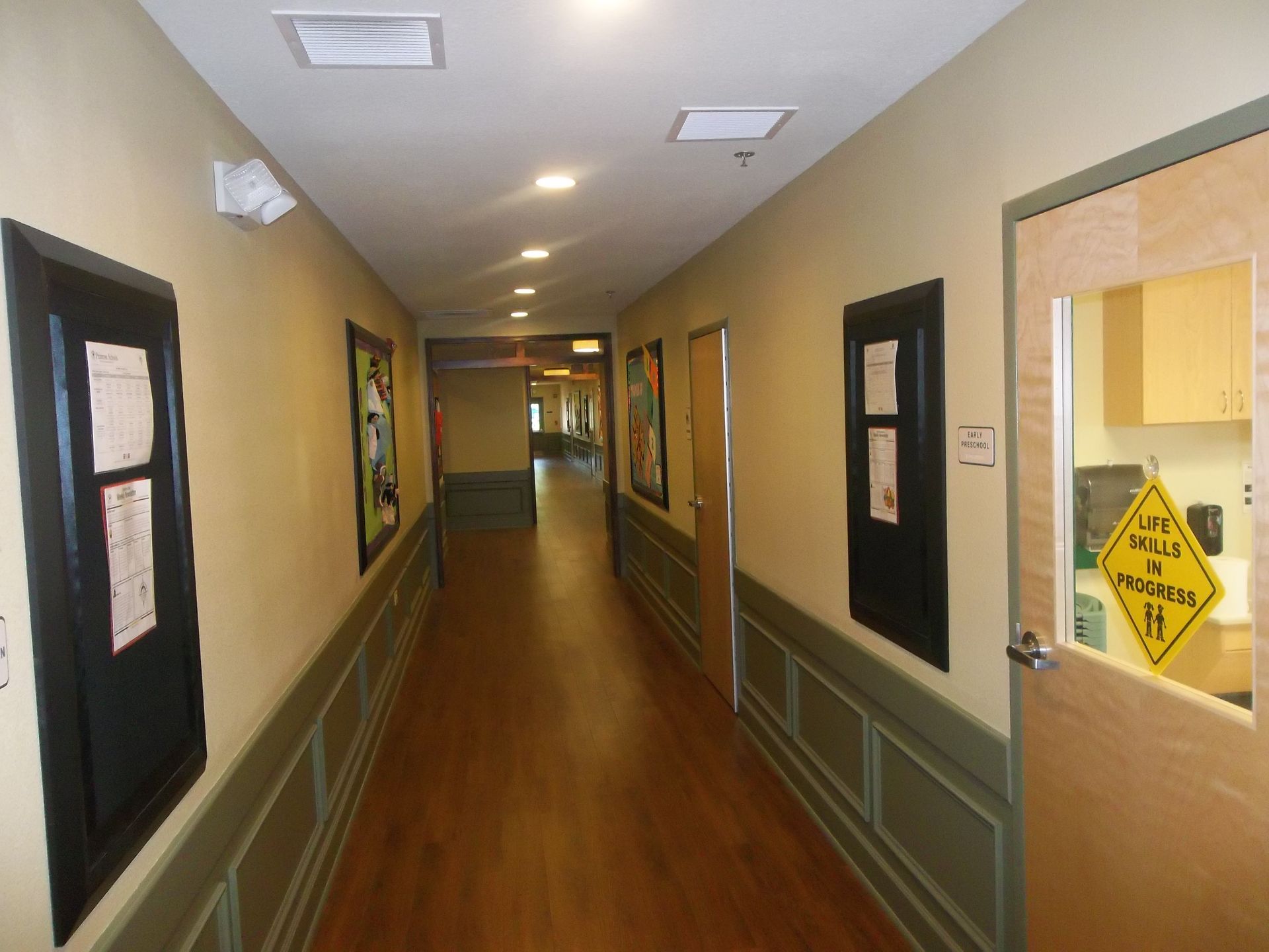 Hallway with wooden floor, beige walls, and closed doors.  Artwork and informational signs are visible.