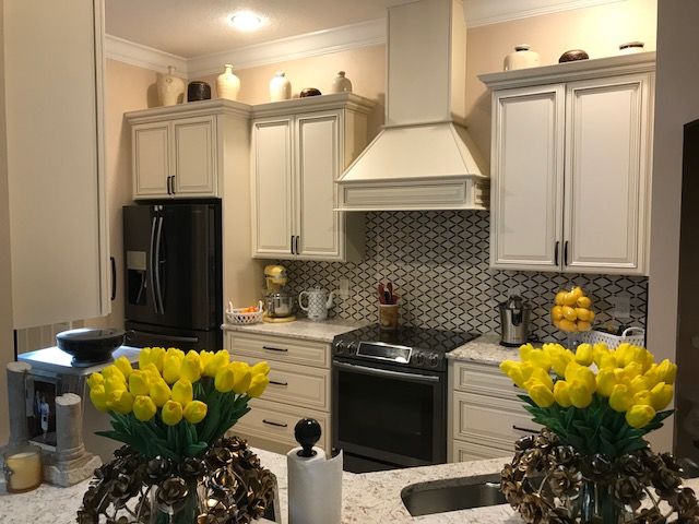 Kitchen with light cabinets, black appliances, mosaic backsplash, and yellow flowers on the counter.