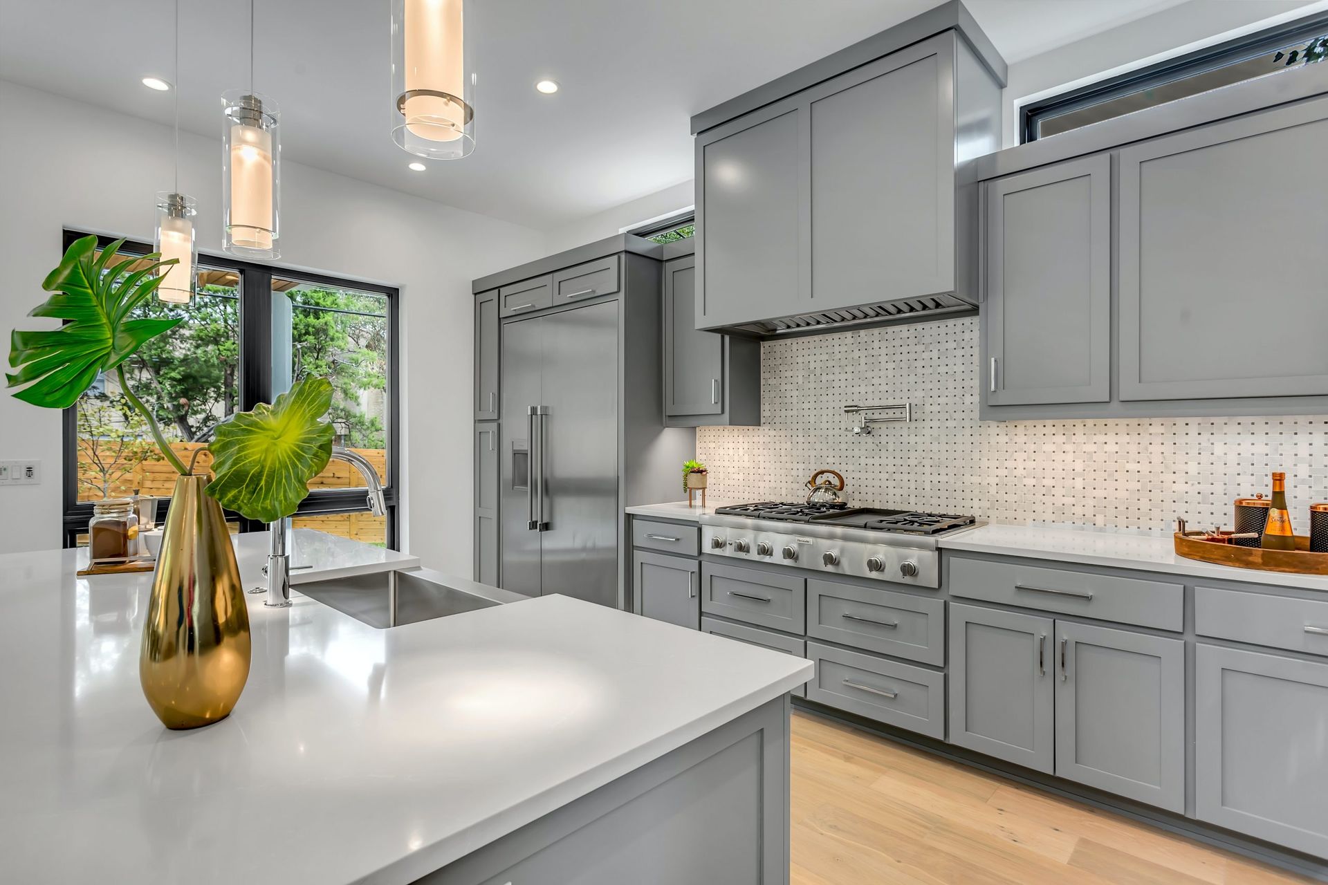 Modern gray kitchen with white countertops, stainless steel appliances, and a gold vase with greenery.