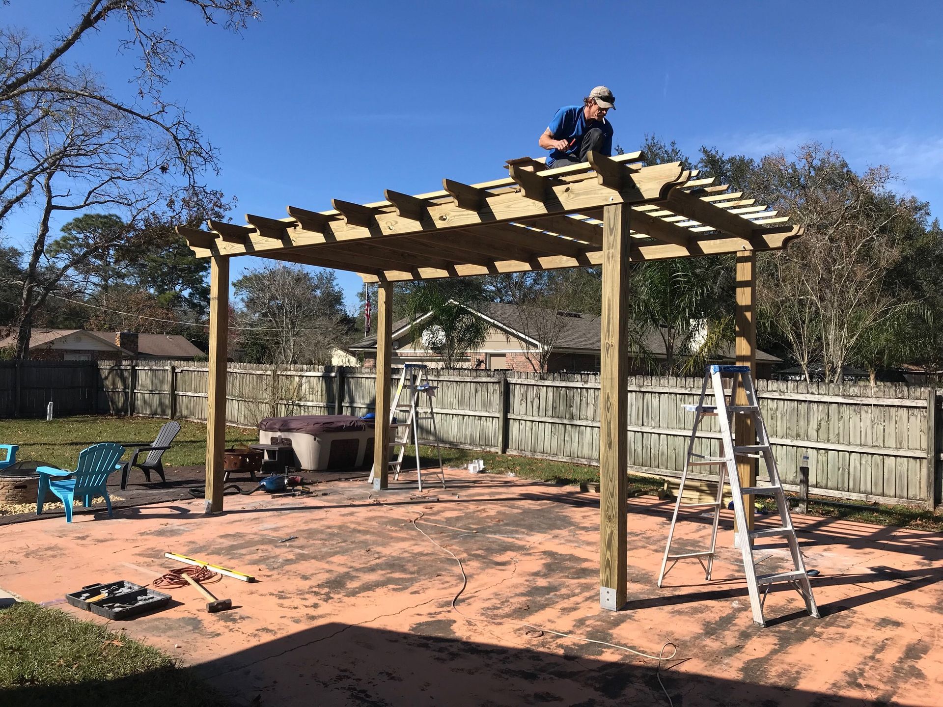 Man on a wooden pergola roof, working on its construction in a backyard.