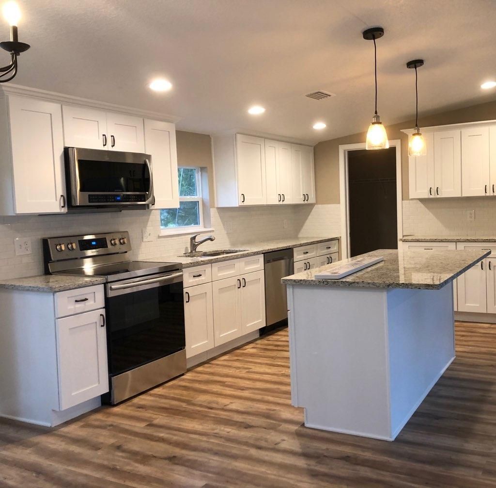Modern kitchen with white cabinets, stainless steel appliances, granite countertops, and wood-look flooring.
