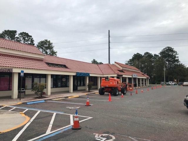 A strip mall with orange cones, a lift, and roof repairs underway on an overcast day.