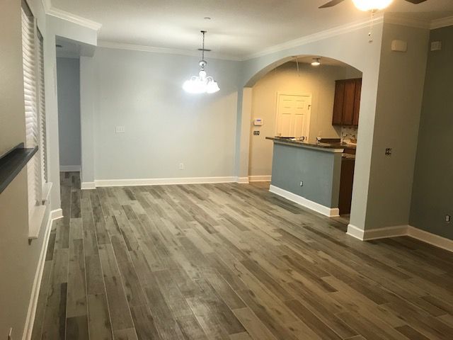 Spacious living room with wood-look flooring, arched doorway to kitchen, and light blue walls.