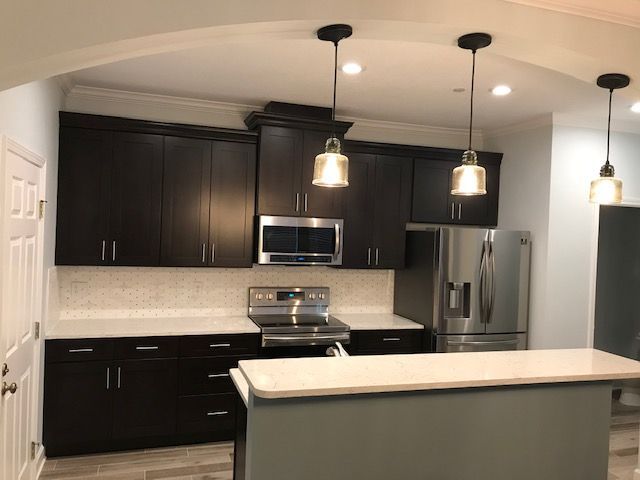 Modern kitchen with dark brown cabinets, stainless steel appliances, and white countertops.