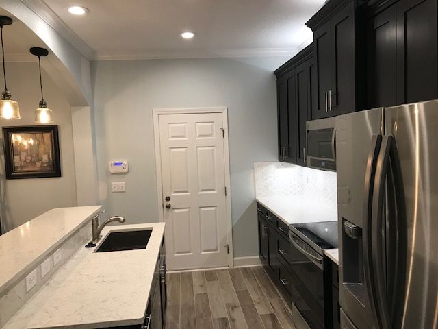 Modern kitchen with dark cabinets, stainless steel appliances, and white countertops.