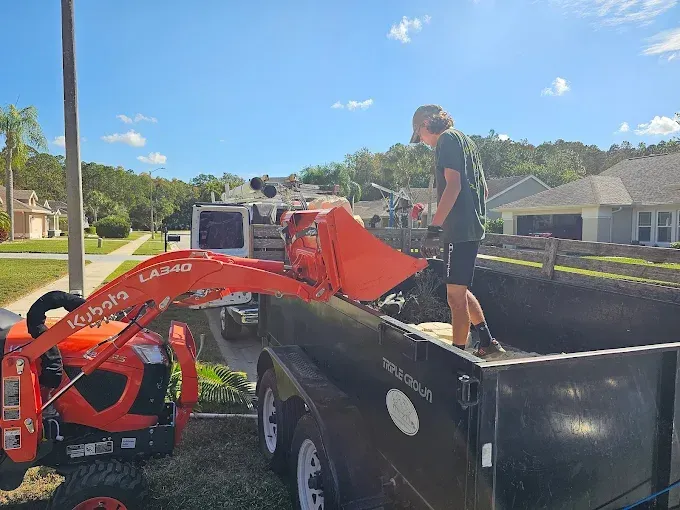 Person loading a red compact excavator into a black trailer on a sunny street