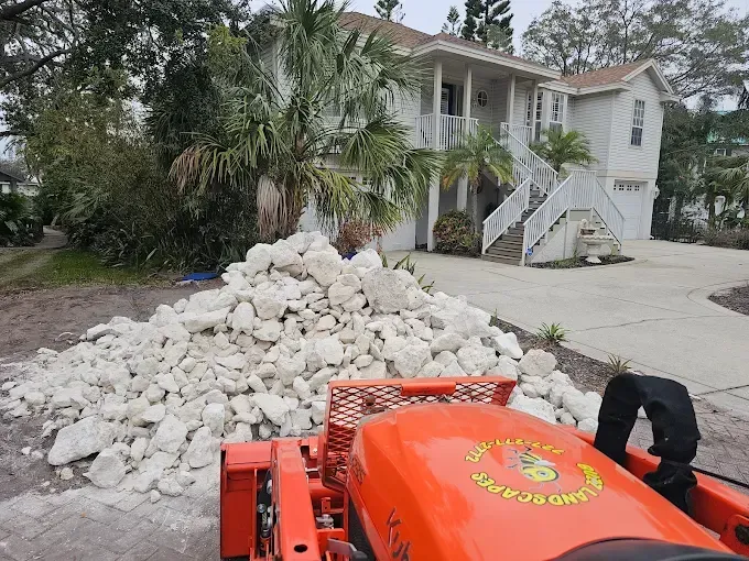 Orange dumpster in front of a house, piled high with white debris and a worker nearby in black pants.
