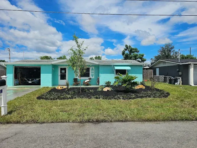 Turquoise single-story house with black mulch landscaping and a blue sky with clouds