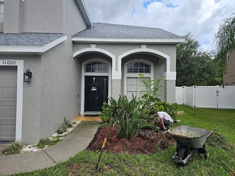 Person gardening in front of a gray house with a black door and white fence