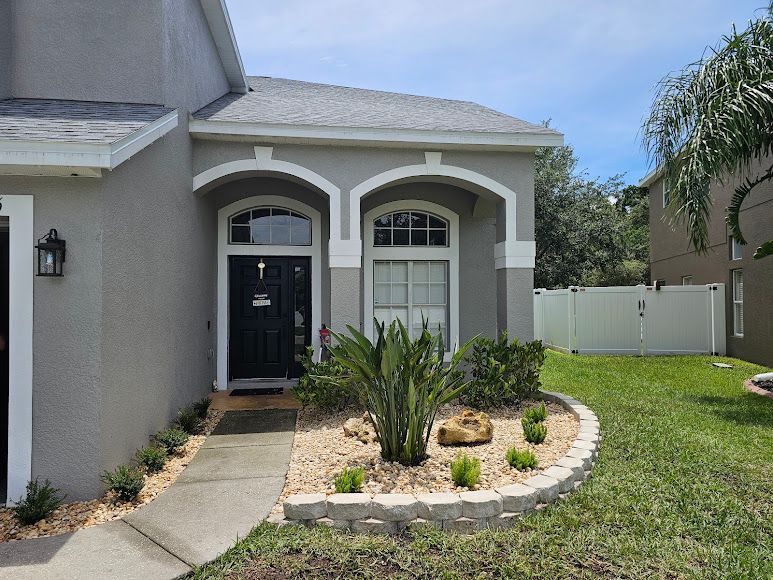 Single-story house exterior with arched front porch, black door, and landscaped front yard