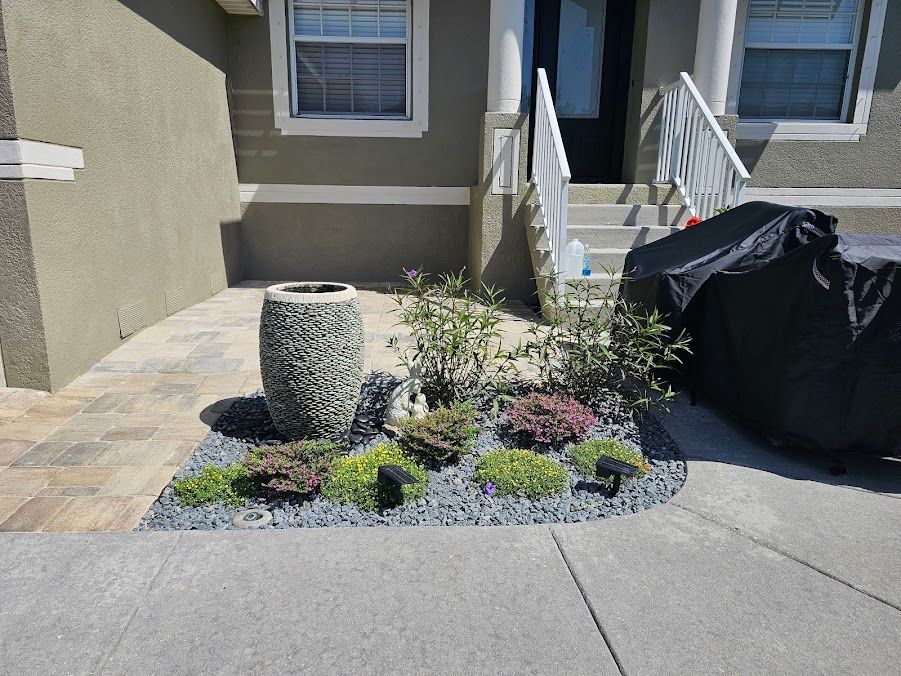 Small desert-style front yard with gravel, succulents, a stone fountain, and a covered grill by the steps.