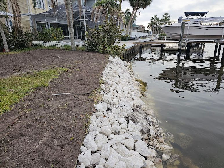 Rock-lined waterfront shoreline beside a dock and calm water under overcast skies