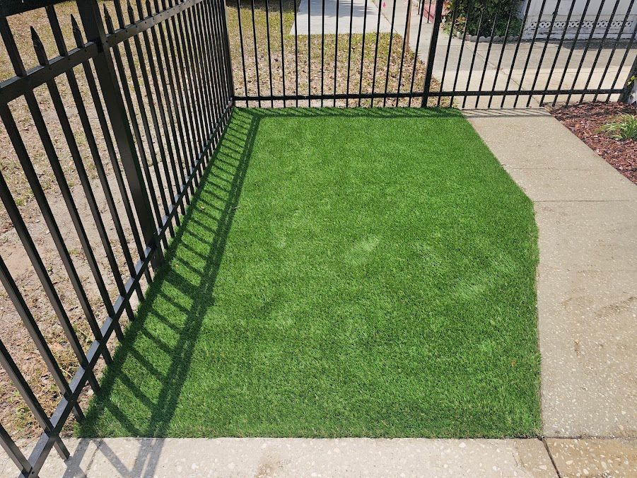 Small fenced yard with bright green artificial grass beside a concrete walkway