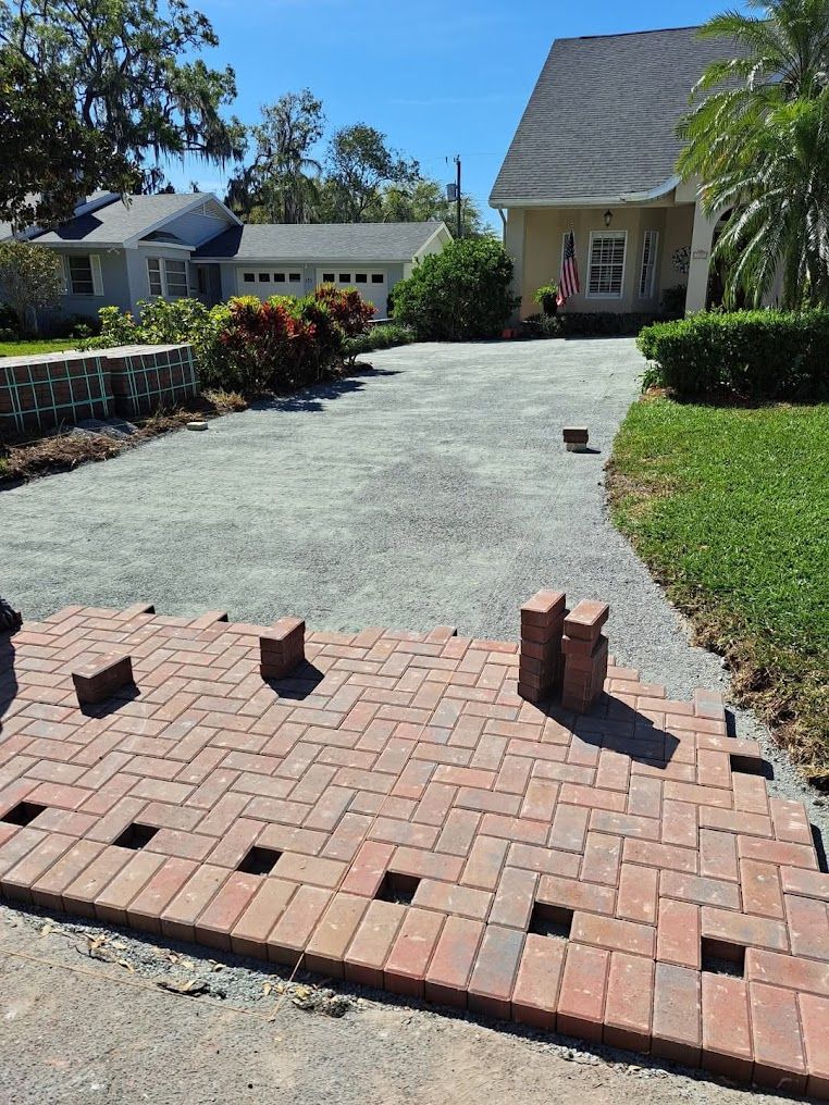 Brick driveway under construction with stacked pavers and a partially paved path beside a house