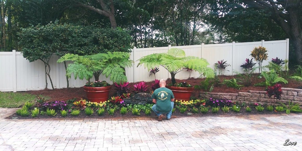 A small blue garden gnome in a colorful flower bed against a white fence.