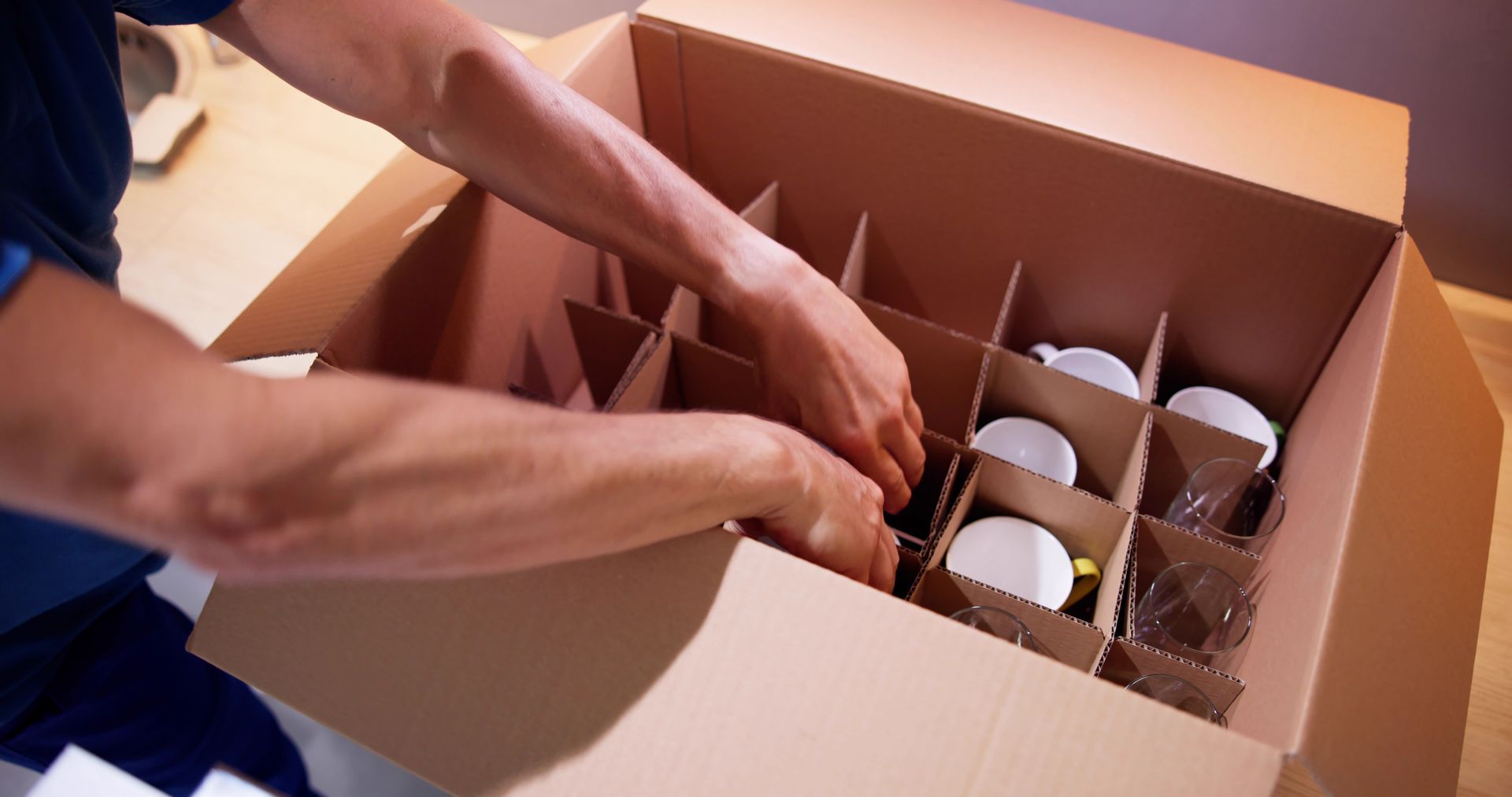 Person packing white cups into a cardboard box with dividers