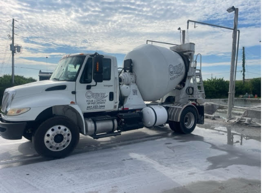White concrete mixer truck parked on a concrete surface, cloudy sky background.