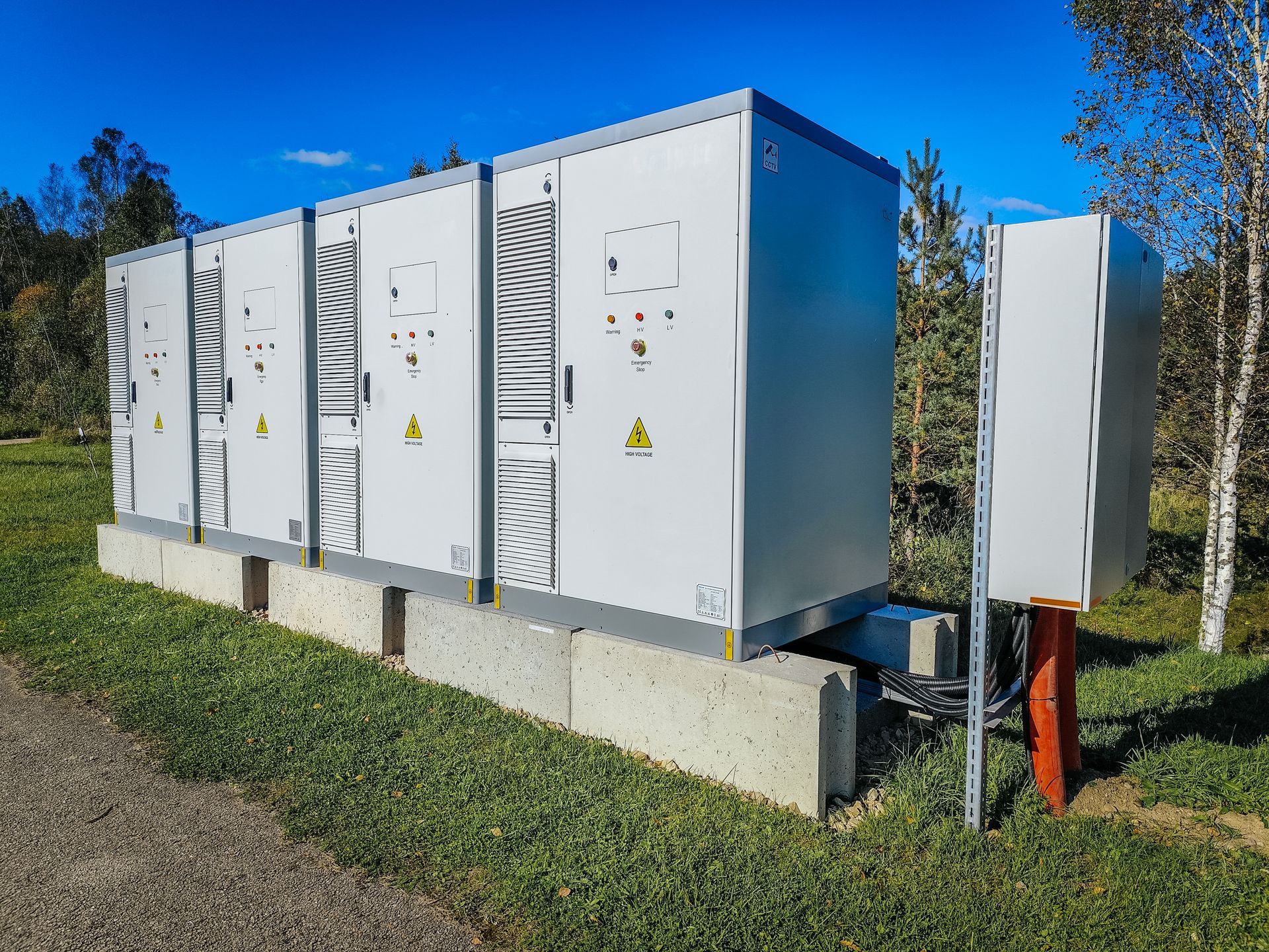 White utility cabinets on a concrete base in a grassy outdoor area under a blue sky